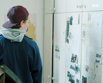 Isak looking at the decorated wall in Even's room.